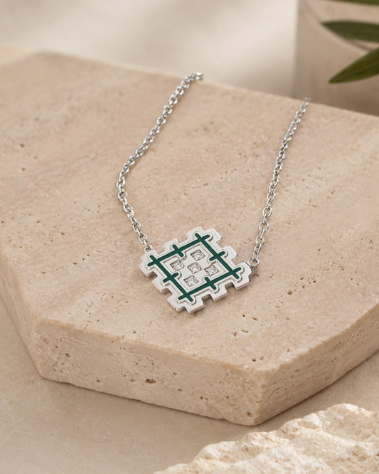 Rhodium-plated sterling silver Lion’s Paw necklace with green enamel, styled on beige travertine stone with a natural green accent.