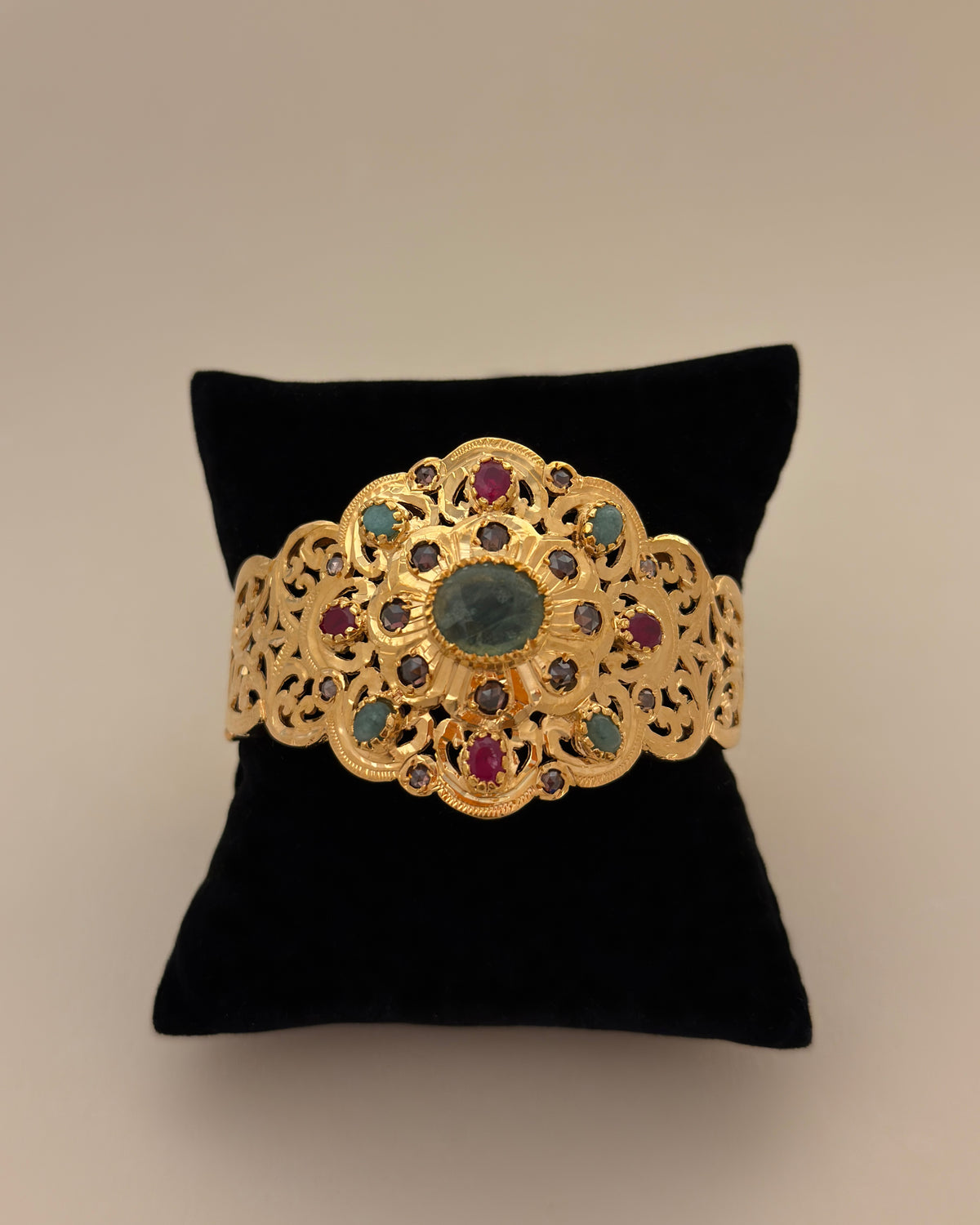 Front view of the gold-plated silver bracelet with a green centre stone, displayed on a black cushion.