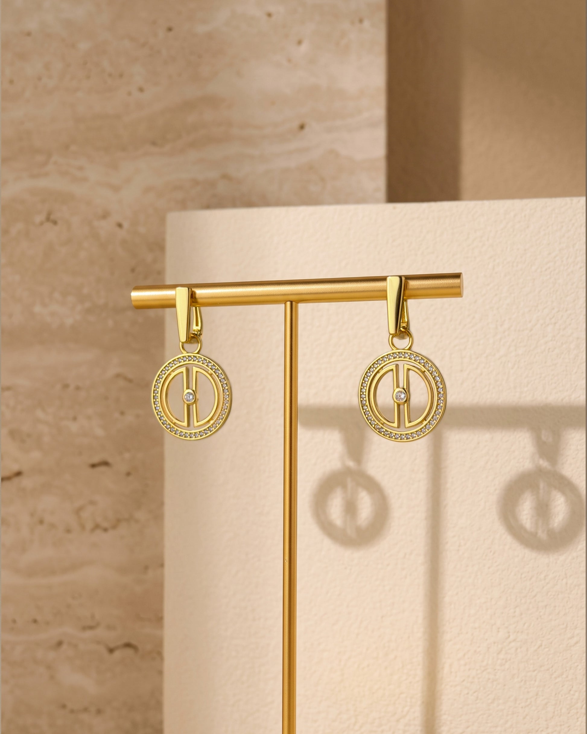 Convertible gold moon earrings displayed on a gold jewelry stand against a beige travertine-inspired background.