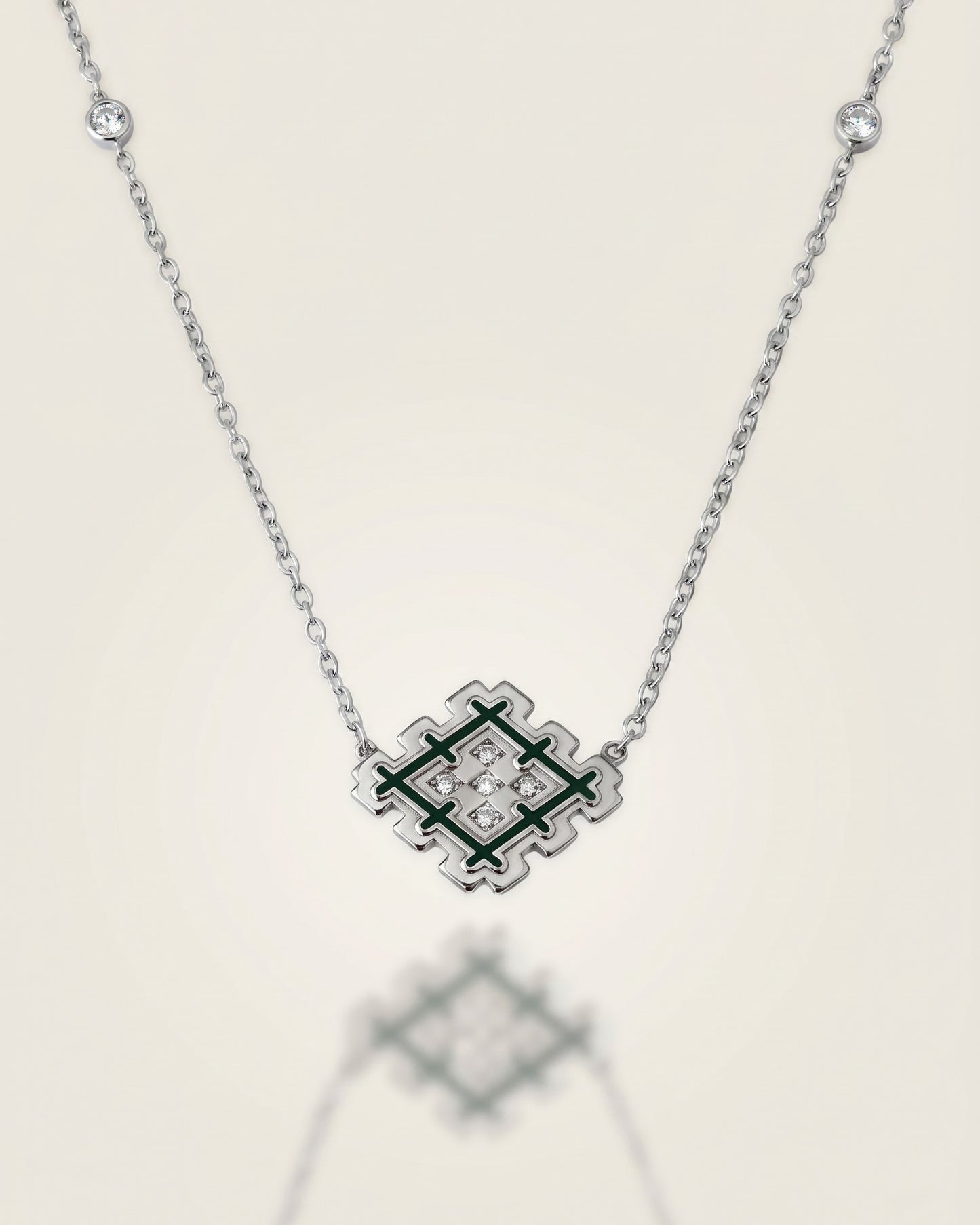Silver Lion’s Paw necklace with green enamel and cubic zirconia details, displayed on a soft neutral background with subtle reflection.