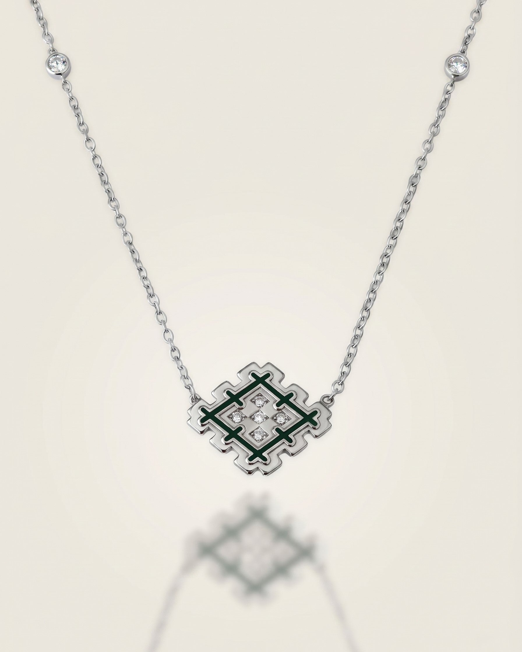 Silver Lion’s Paw necklace with green enamel and cubic zirconia details, displayed on a soft neutral background with subtle reflection.