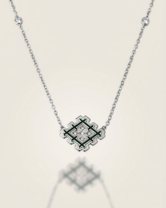Silver Lion’s Paw necklace with green enamel and cubic zirconia details, displayed on a soft neutral background with subtle reflection.