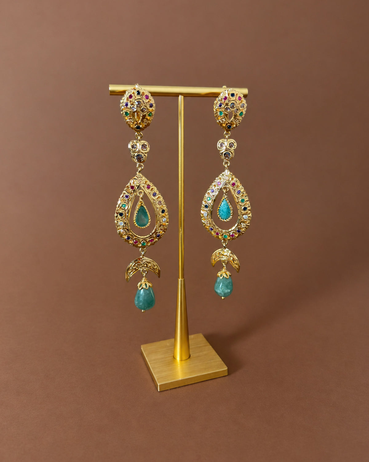 Pair of handmade Moroccan sterling silver drop earrings with green cabochons hanging from a gold-coloured display stand.
