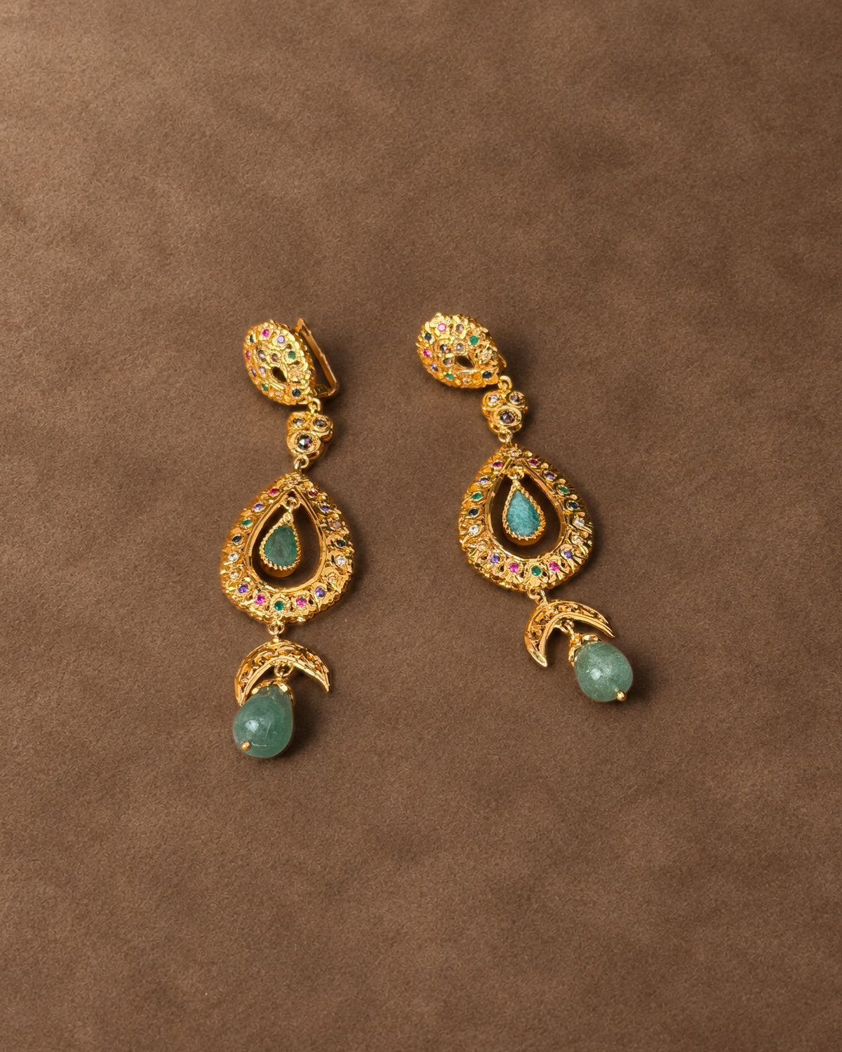 Gold-plated sterling silver earrings from Fez laid on a brown surface, showing multicoloured stones and green cabochon drops.