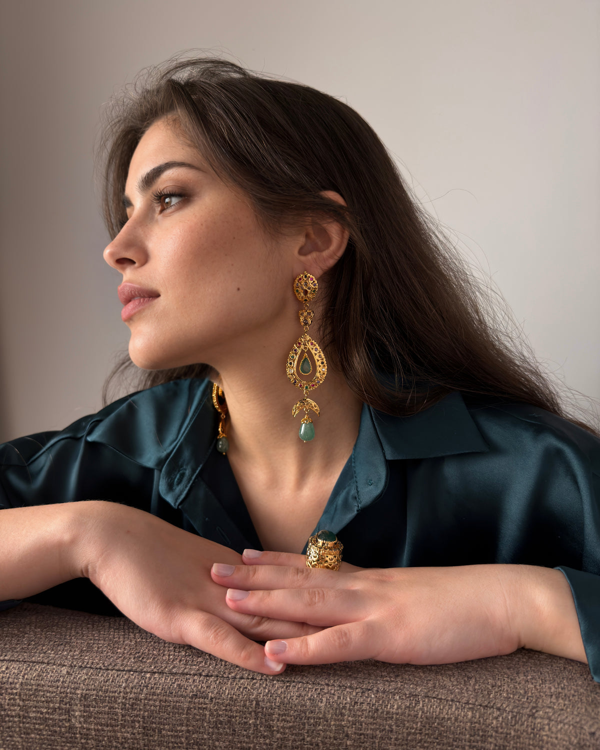 Seated model wearing handmade Moroccan drop earrings with green cabochons and a teal satin shirt.