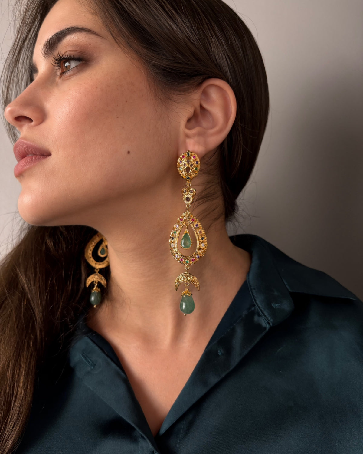Close-up of a Moroccan drop earring worn in profile, showing openwork teardrop details and a green cabochon.
