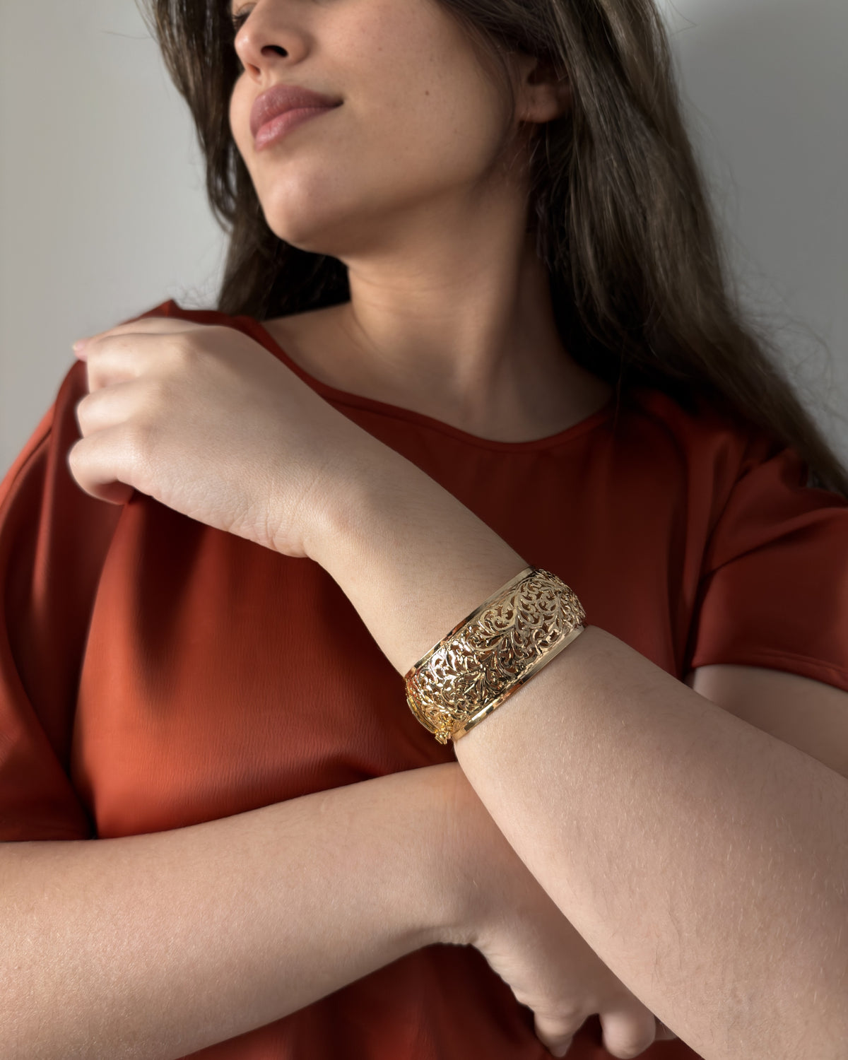 Model wearing the wide Arabesque bracelet with a terracotta blouse, her forearm raised across her chest.