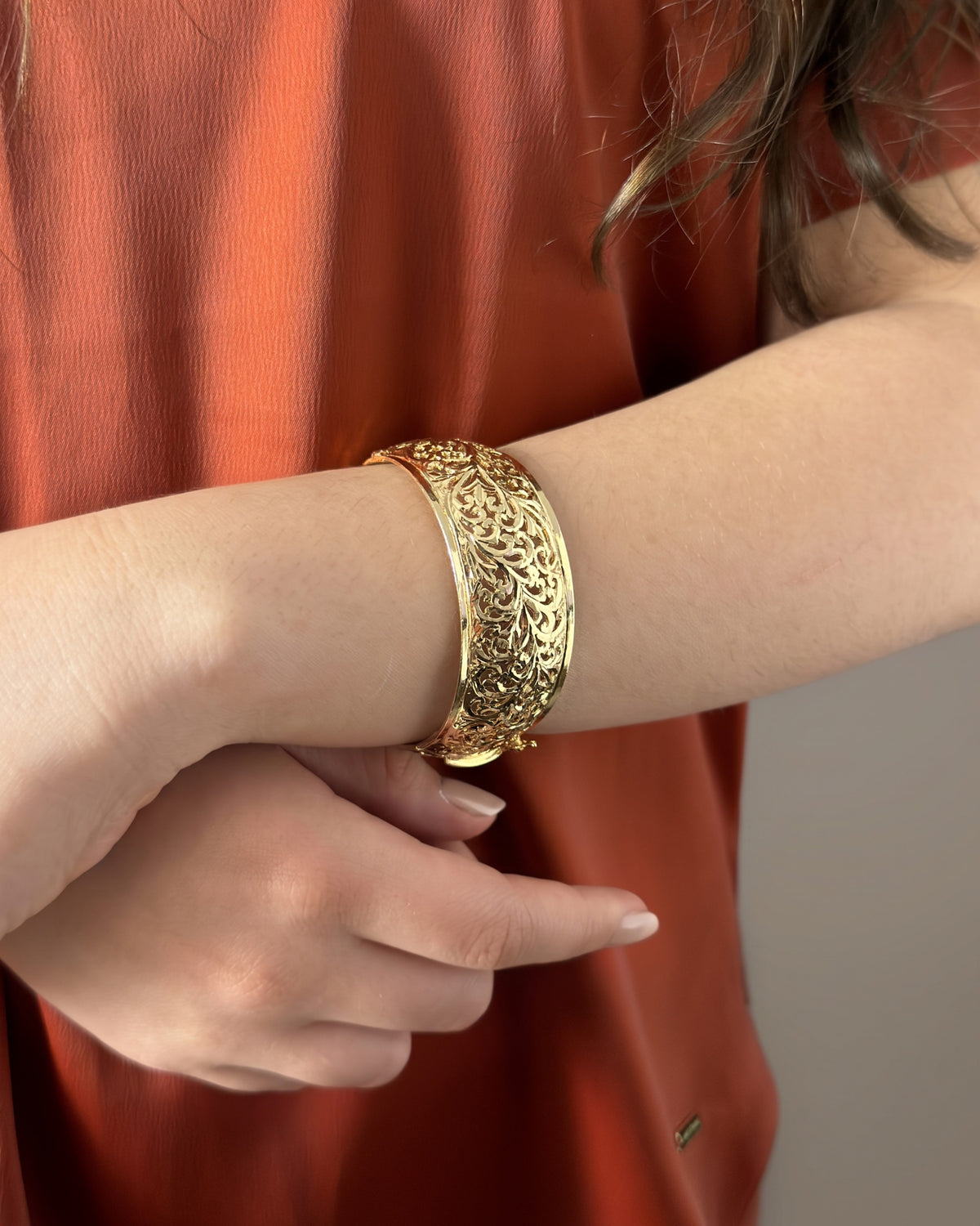 Close-up of the Arabesque openwork bracelet worn on the wrist, with a terracotta blouse in the background.