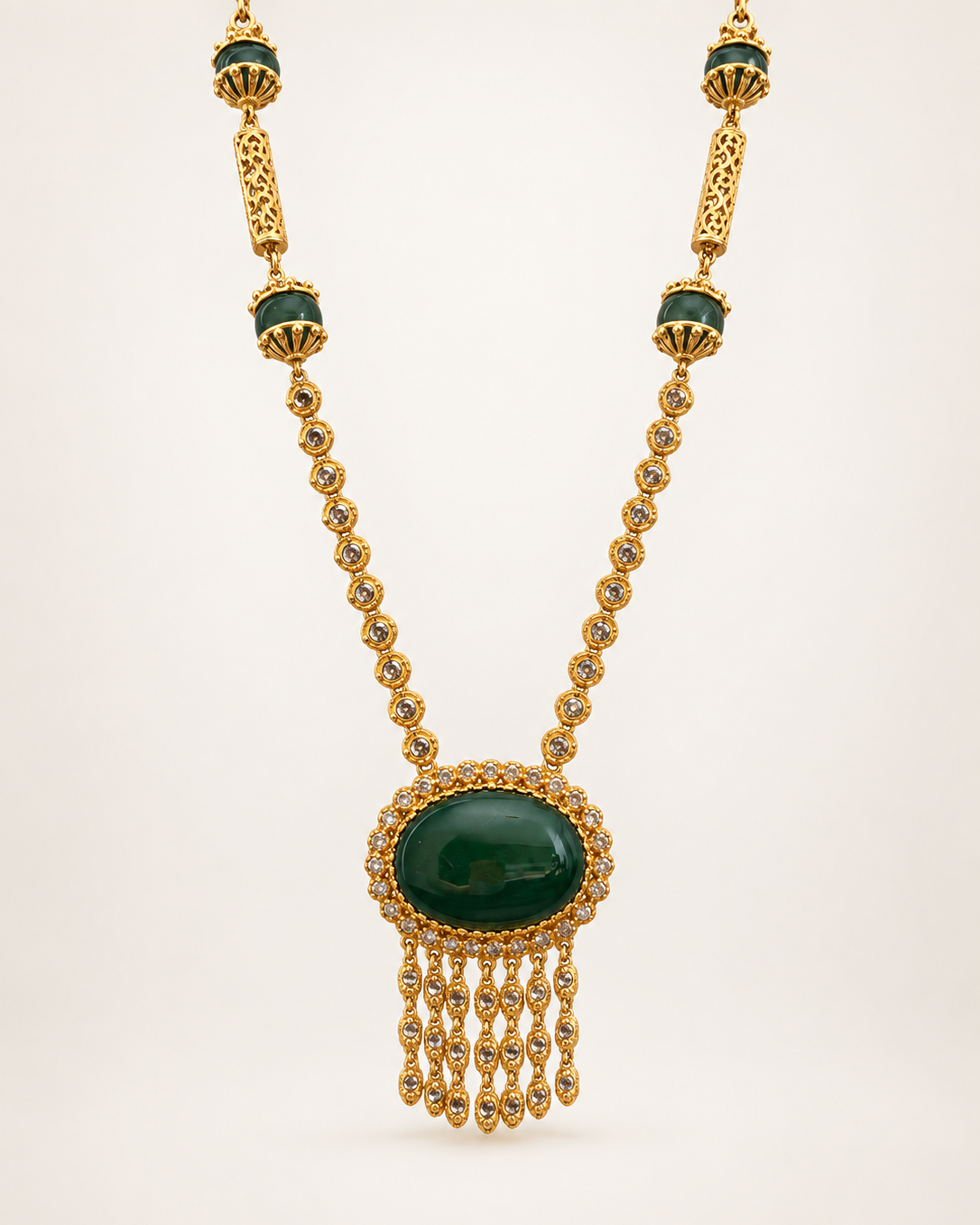 Gold-plated long necklace with detailed pendant, front view on a soft beige gradient background