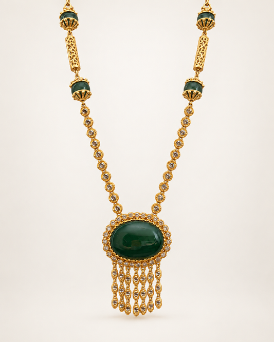 Gold-plated long necklace with detailed pendant, front view on a soft beige gradient background