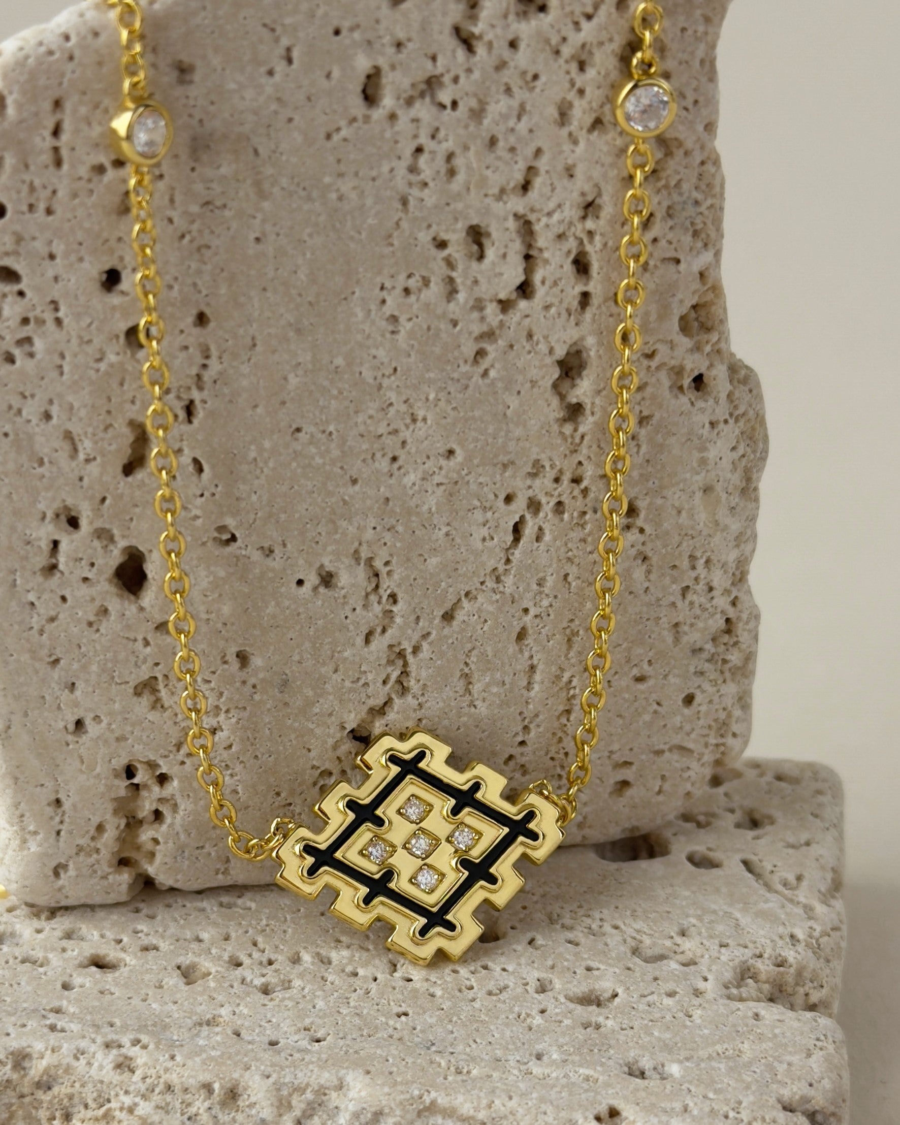Close-up of a black enamel Lion’s Paw necklace in gold vermeil, styled on beige travertine stone with geometric pendant details.