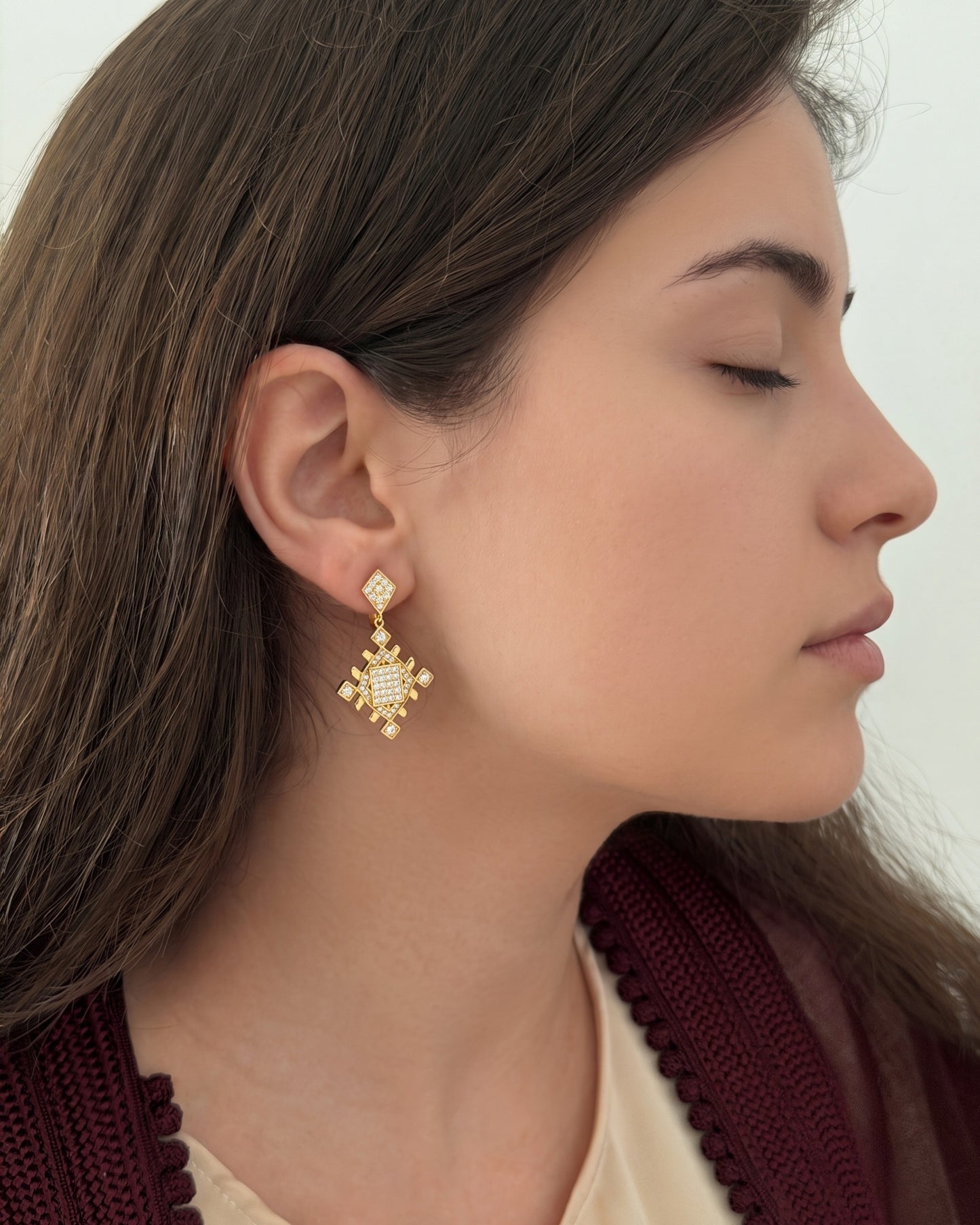 Woman wearing gold Lion’s Paw statement earrings inspired by Amazigh symbolism, styled with a burgundy Moroccan-inspired outfit.