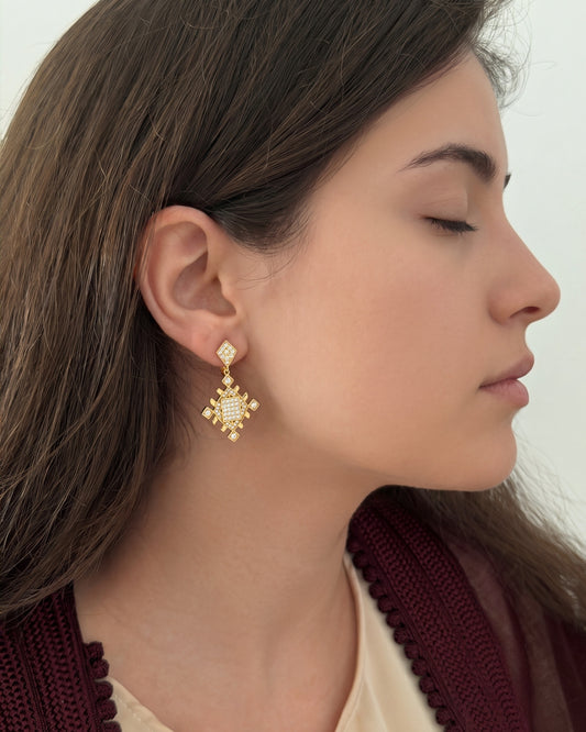 Woman wearing gold Lion’s Paw statement earrings inspired by Amazigh symbolism, styled with a burgundy Moroccan-inspired outfit.