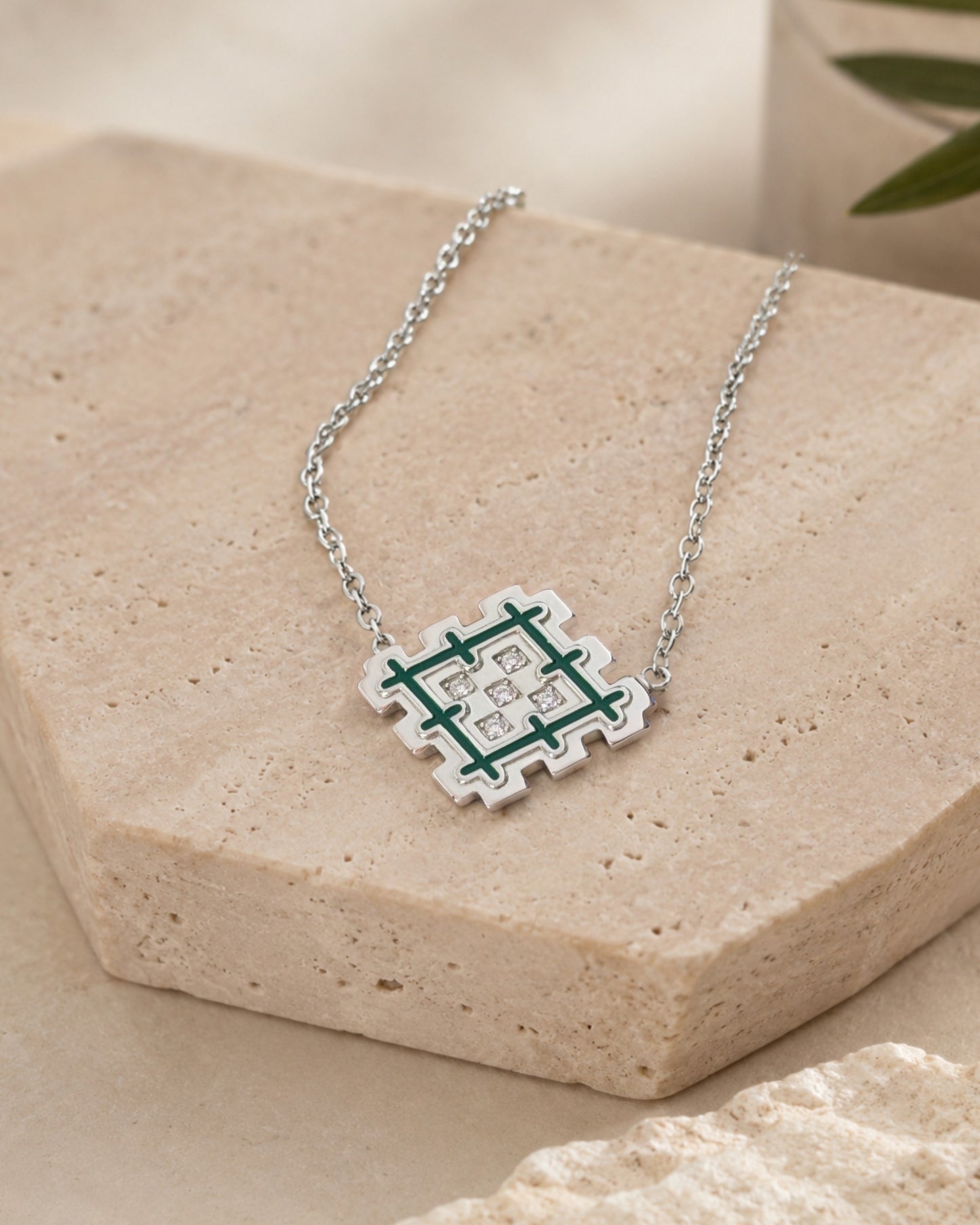 Rhodium-plated sterling silver Lion’s Paw necklace with green enamel, styled on beige travertine stone with a natural green accent.