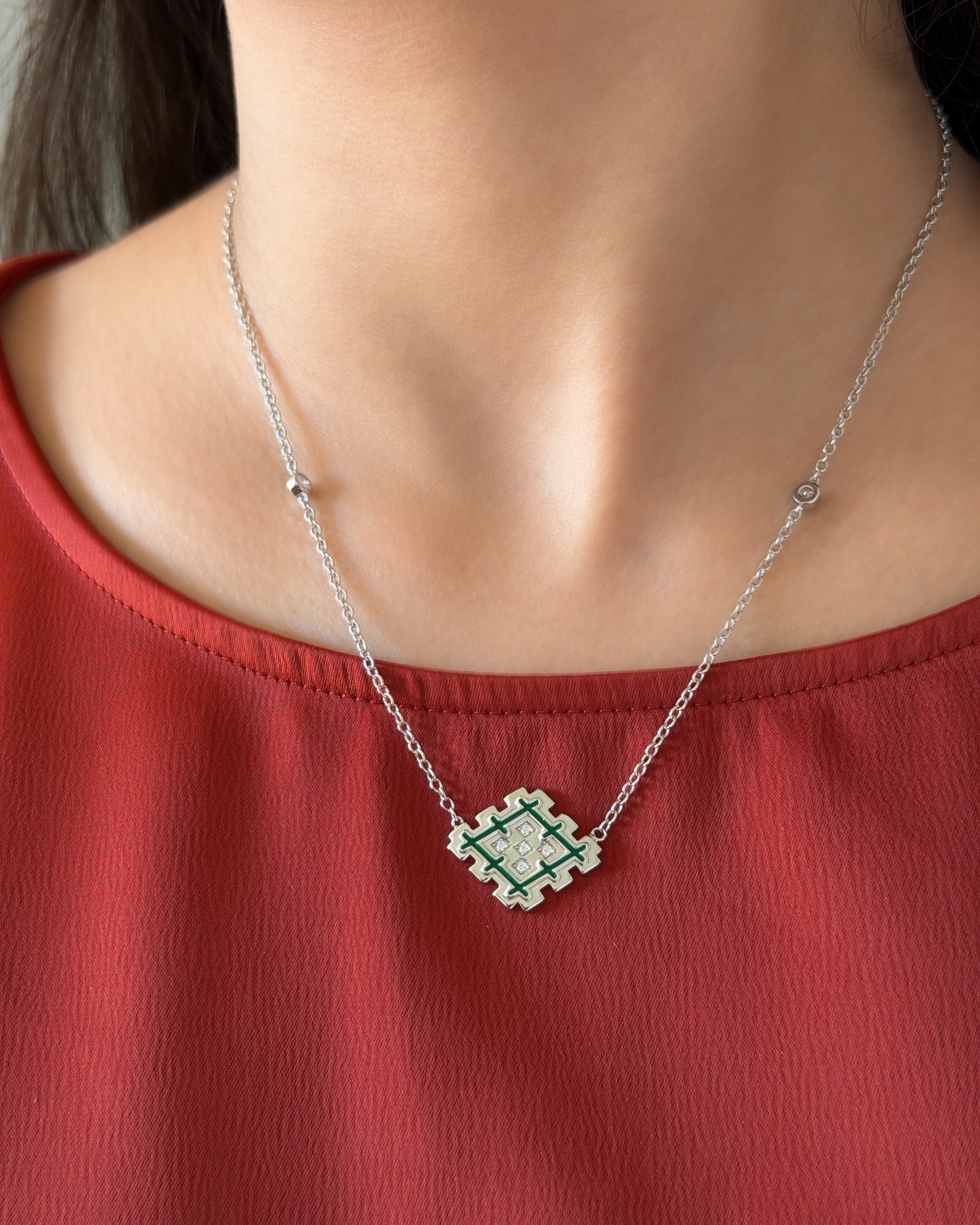 Lifestyle photo of a woman wearing a silver Lion’s Paw green enamel necklace with a terracotta top, showing the necklace worn naturally.