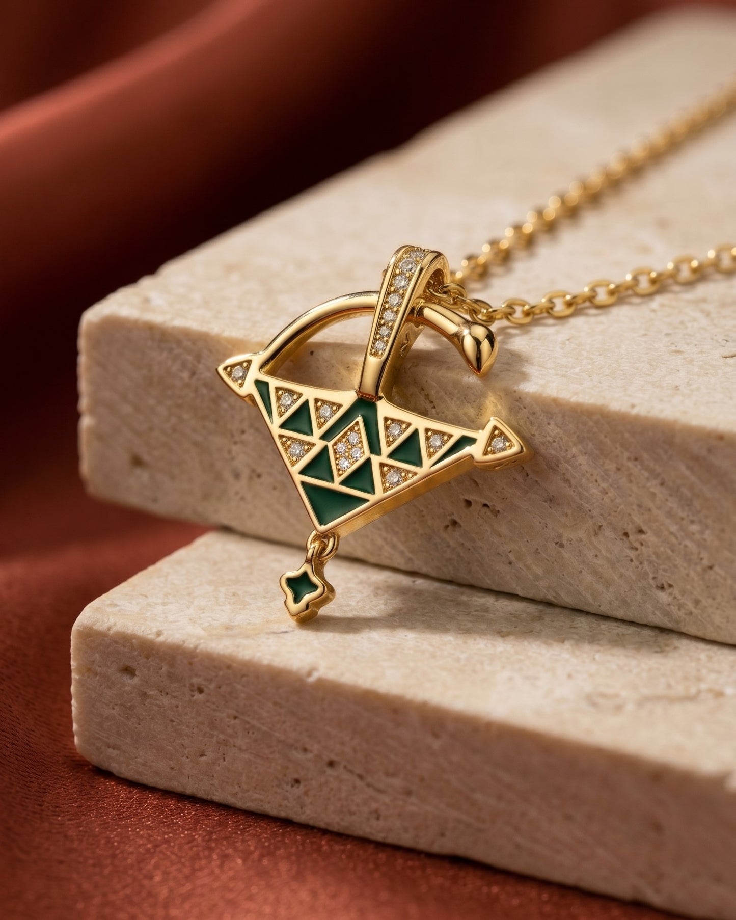 Close-up product photo of a gold vermeil Tizerzit pendant with green enamel and sparkling zirconia stones styled on beige travertine stone.