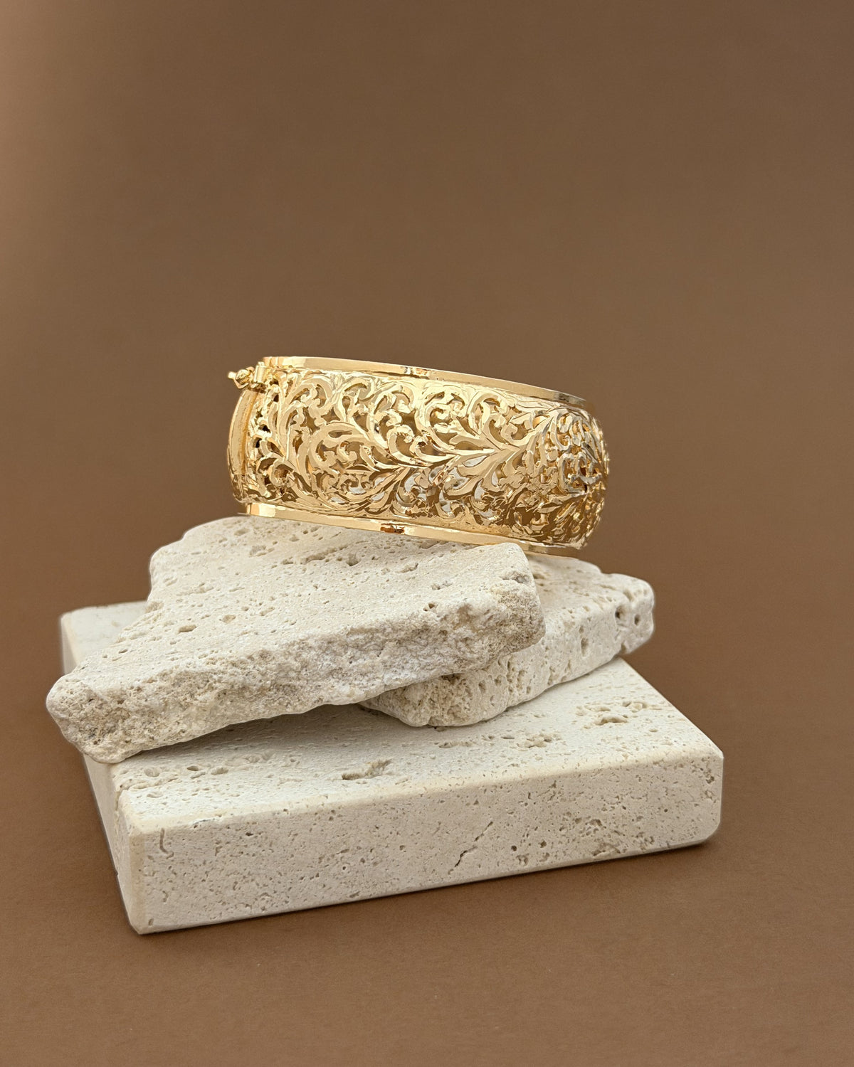 Arabesque bracelet with botanical openwork displayed on stacked pale stones against a warm brown background.