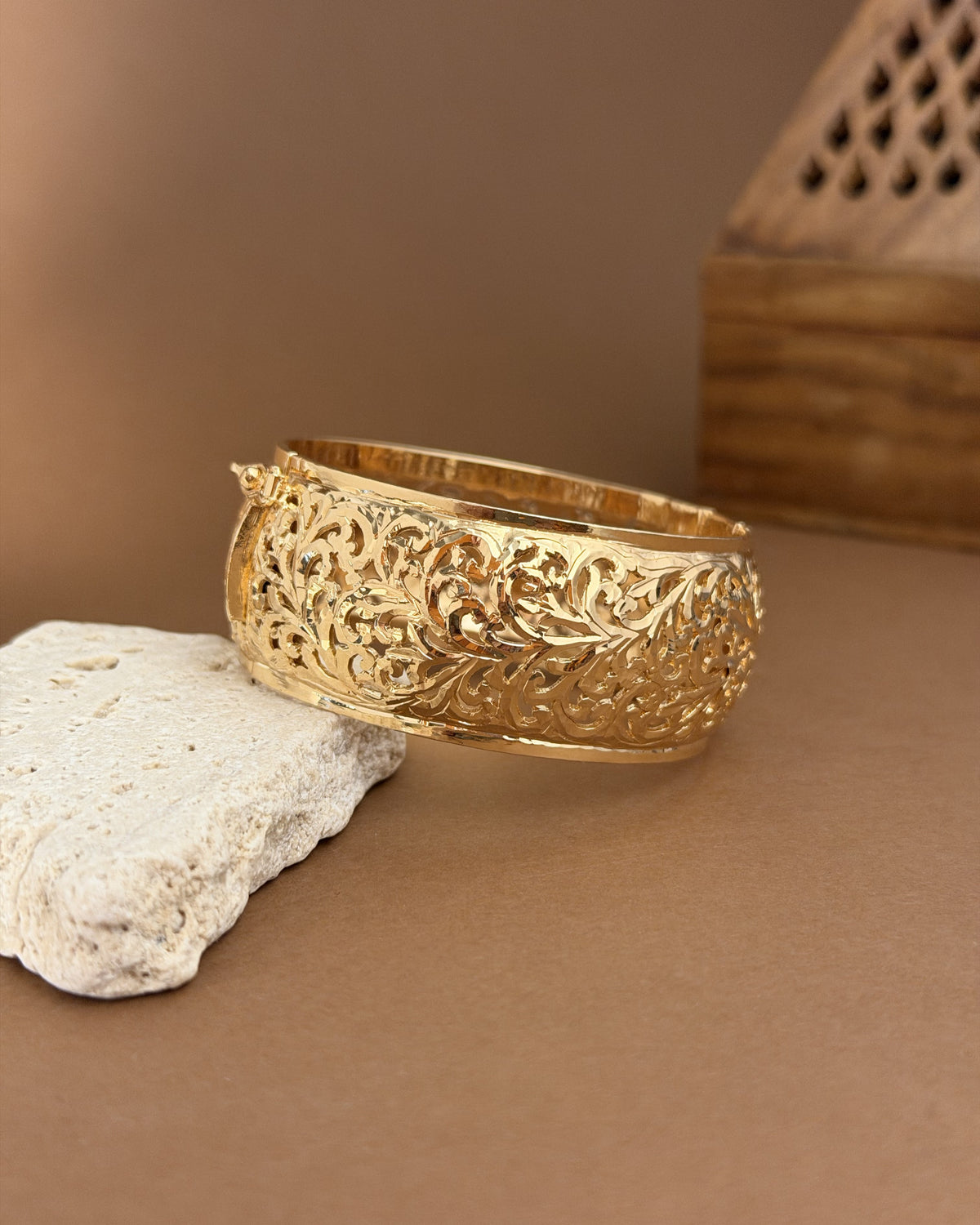 Angled view of the Arabesque gold-plated silver bracelet resting on a pale stone, showing its openwork and curved shape.