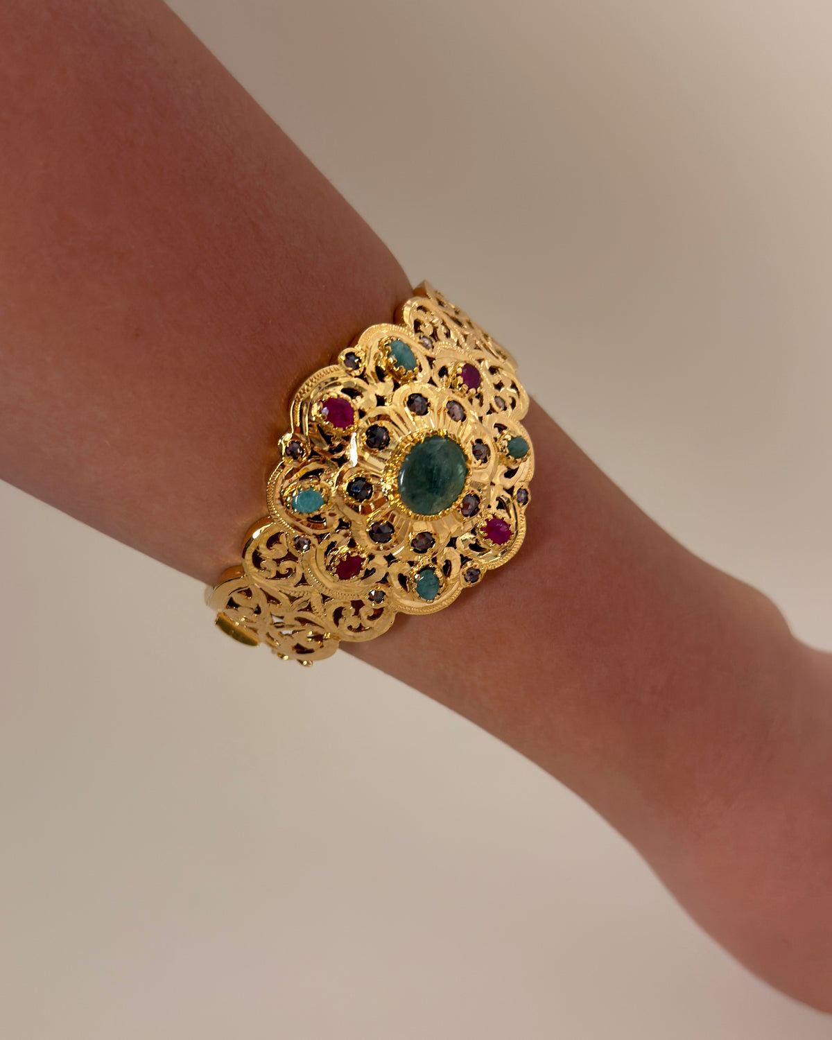 Gold-plated silver rosette bracelet with green, red and pink stones, shown on a wrist.
