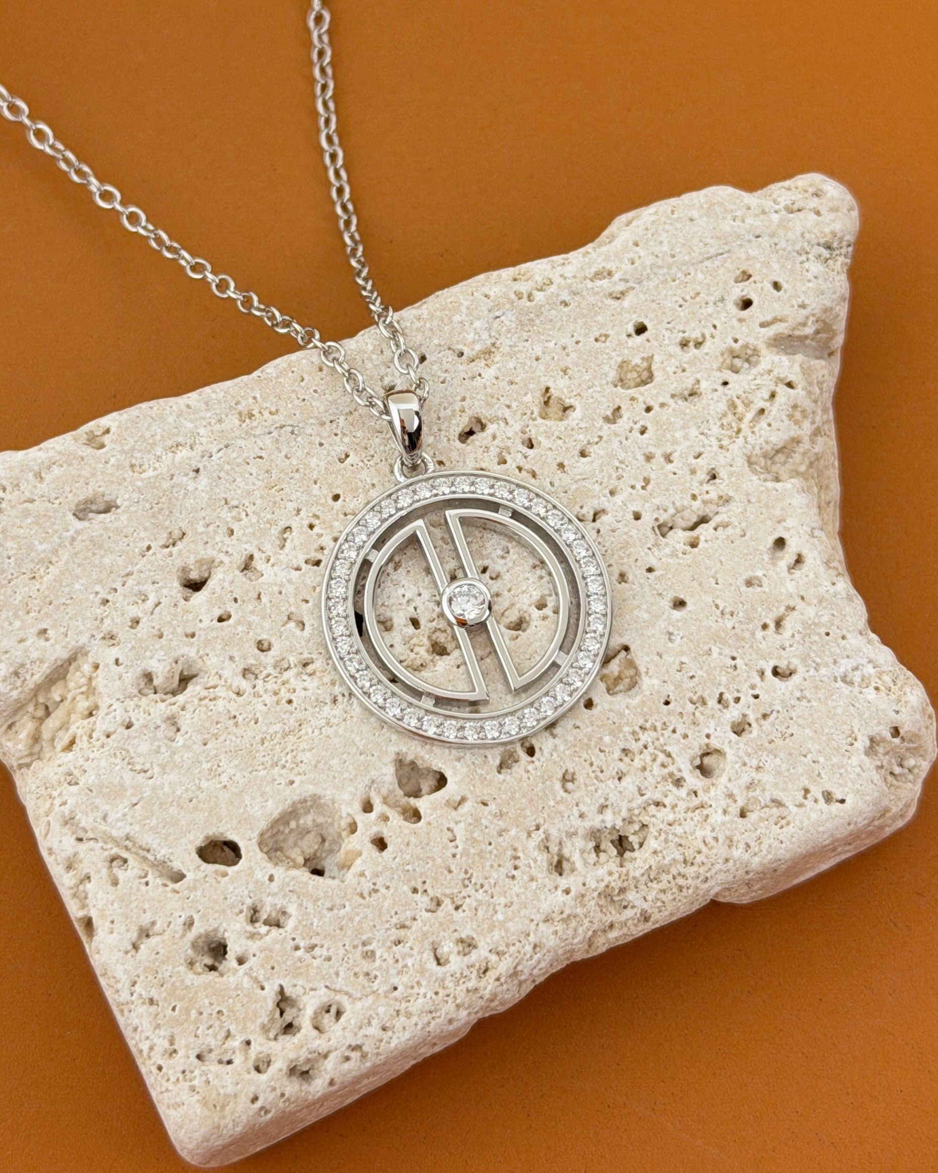 Rhodium-plated sterling silver moon necklace styled on beige travertine stone with a warm terracotta background.