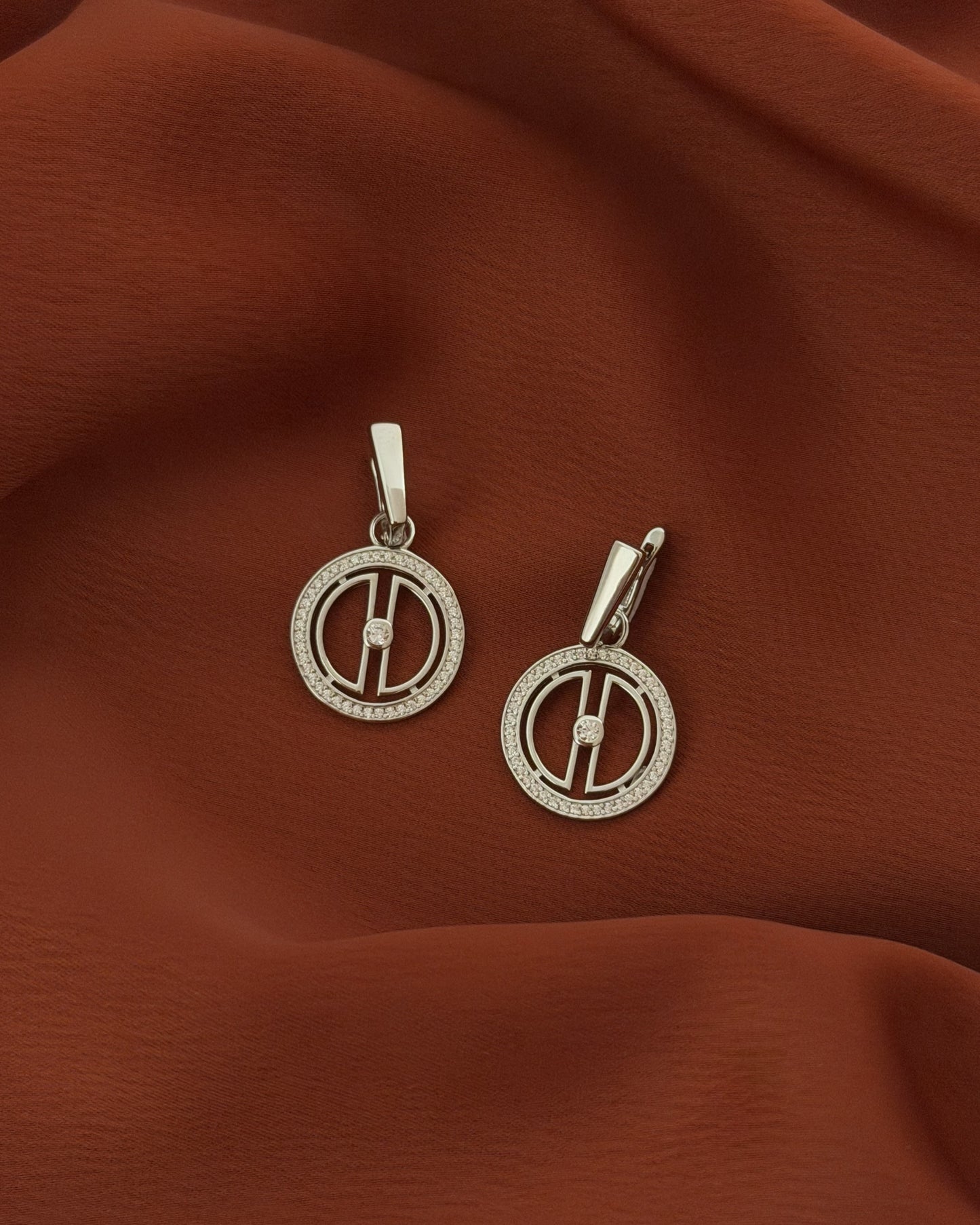 Rhodium-plated sterling silver moon drop earrings styled on warm terracotta fabric, featuring a celestial design with cubic zirconia stones.