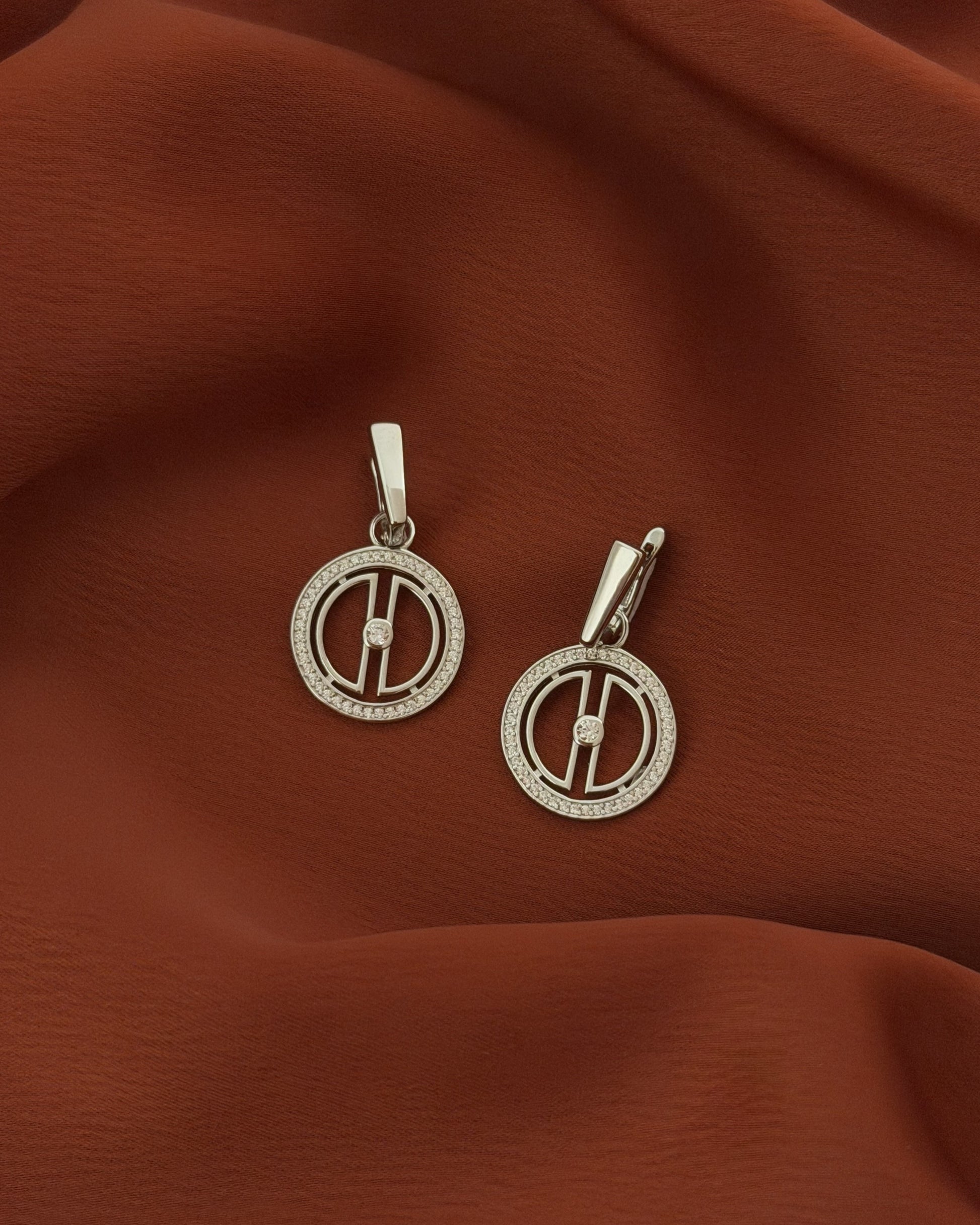 Rhodium-plated sterling silver moon drop earrings styled on warm terracotta fabric, featuring a celestial design with cubic zirconia stones.