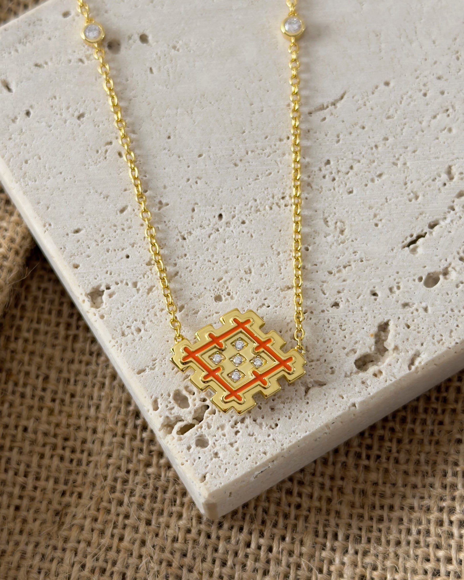 Close-up of an orange enamel Lion’s Paw necklace in gold vermeil, styled on beige travertine stone with cubic zirconia details.