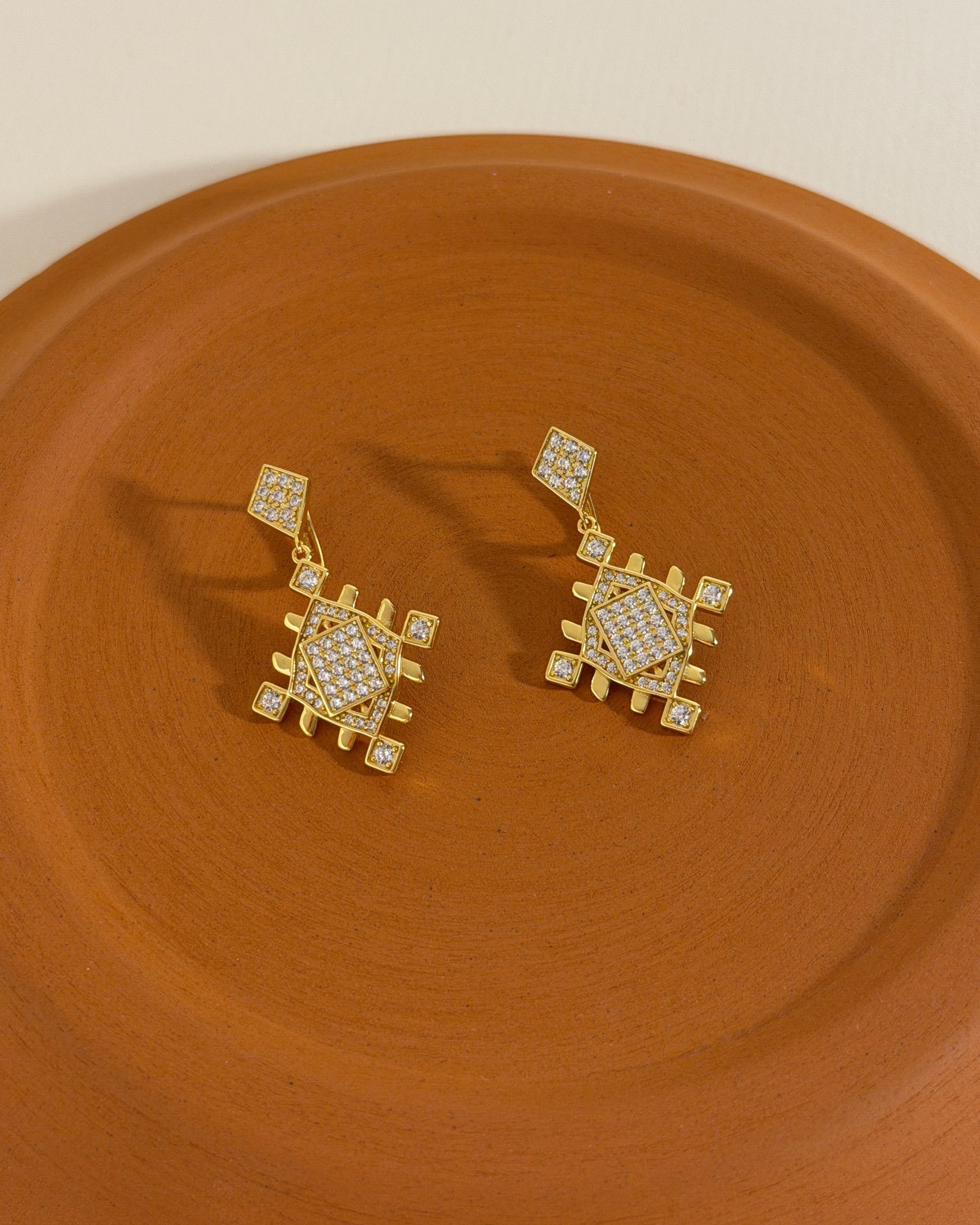 Close-up of gold vermeil Lion’s Paw earrings with cubic zirconia details styled on a warm terracotta surface.