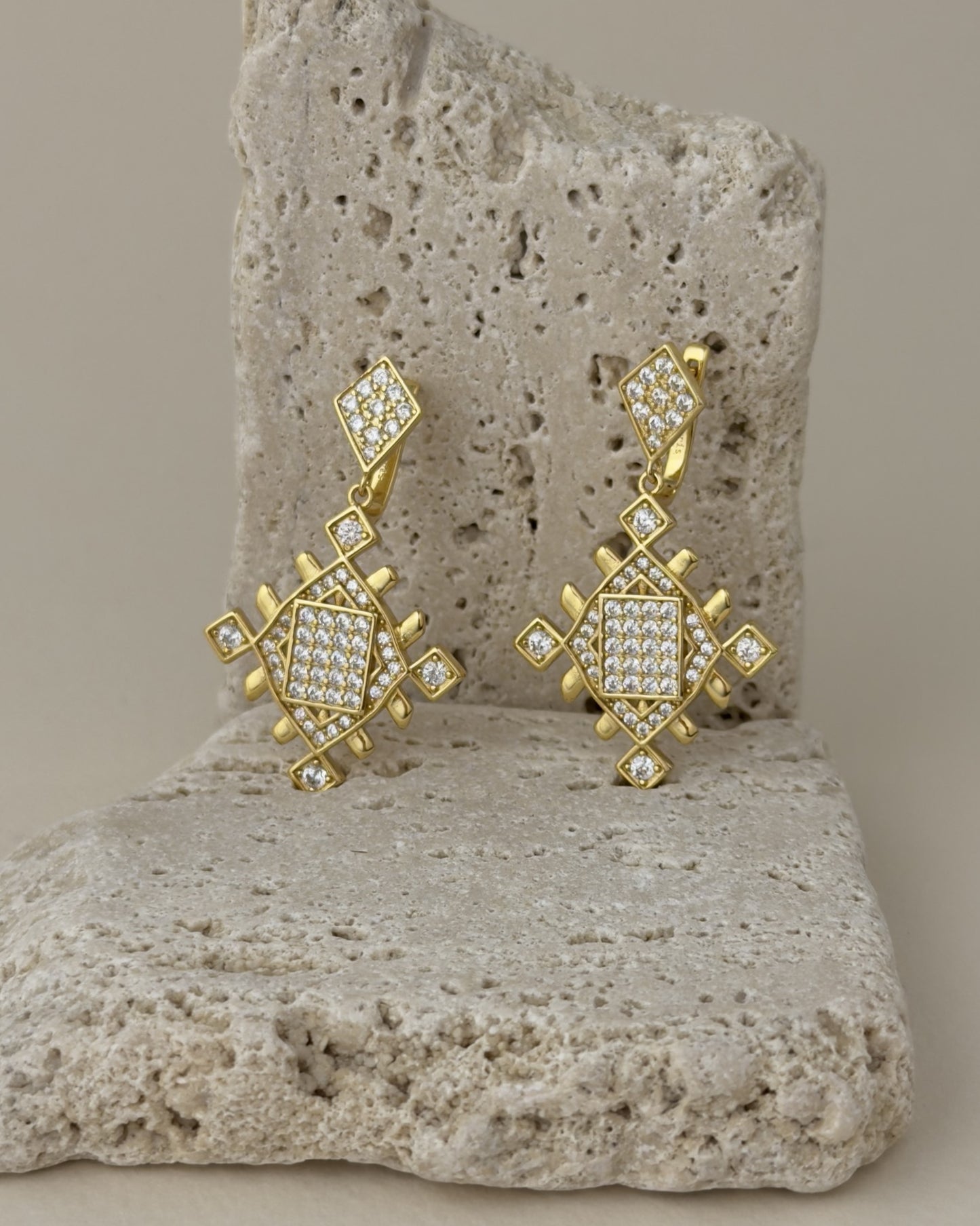 Gold Lion’s Paw statement earrings with cubic zirconia details displayed on beige travertine stone for a luxury jewelry look.