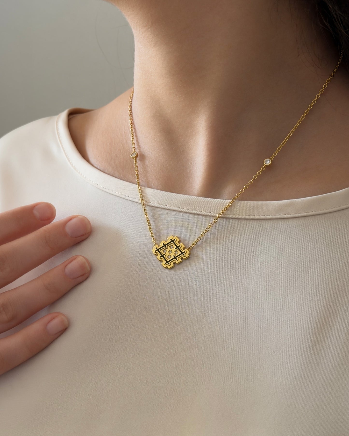 Woman wearing a gold vermeil Lion’s Paw necklace with black enamel, styled on a light satin top for an elegant everyday look.