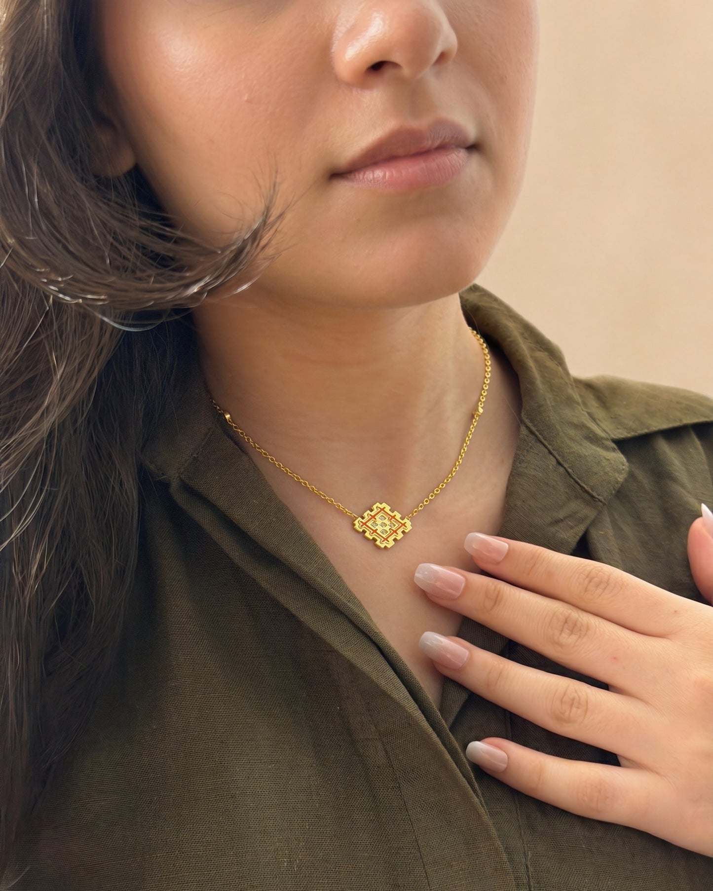 Lifestyle photo of a gold vermeil Lion’s Paw necklace with orange enamel worn with an olive shirt, highlighting the warm symbolic pendant.