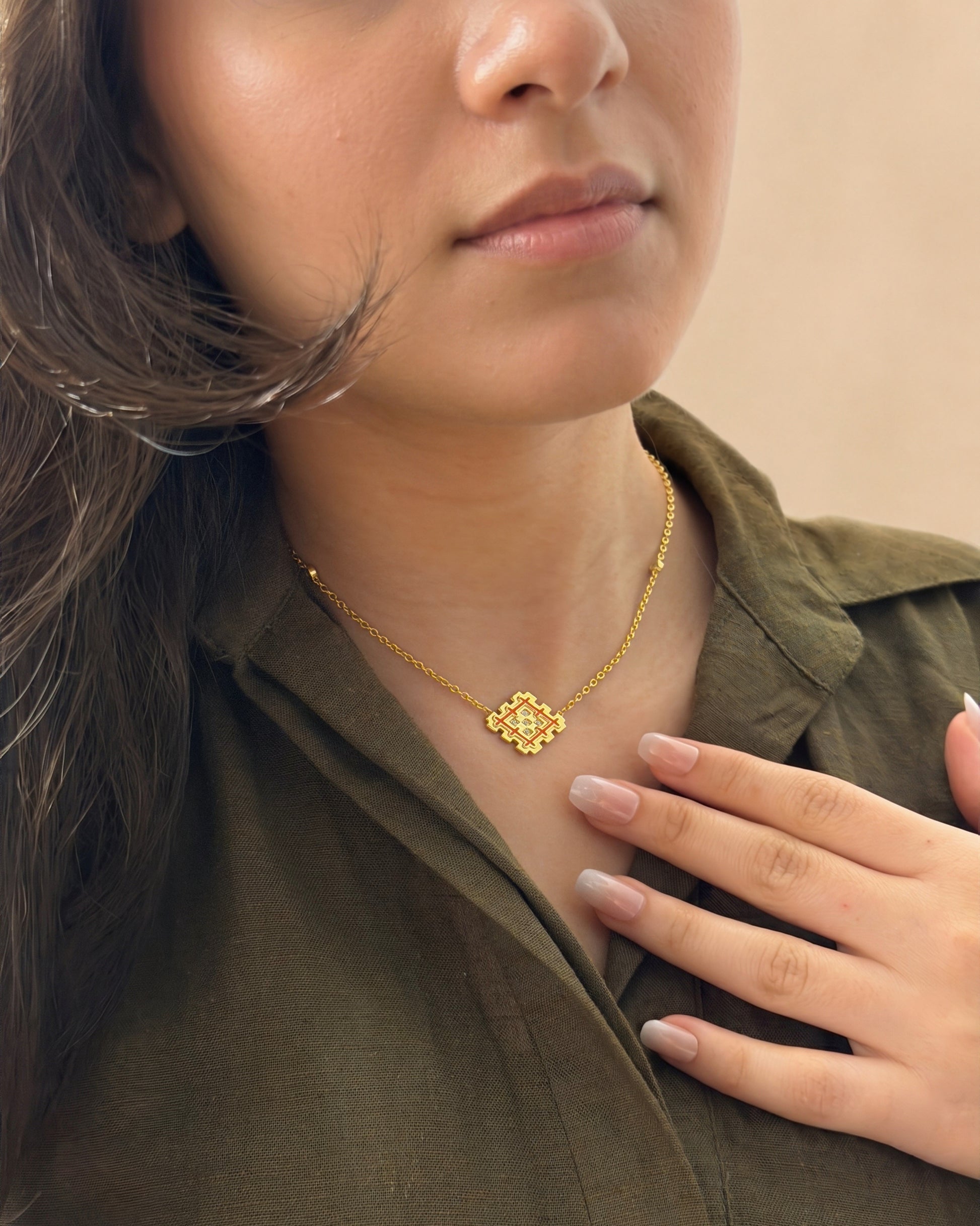 Lifestyle photo of a gold vermeil Lion’s Paw necklace with orange enamel worn with an olive shirt, highlighting the warm symbolic pendant.