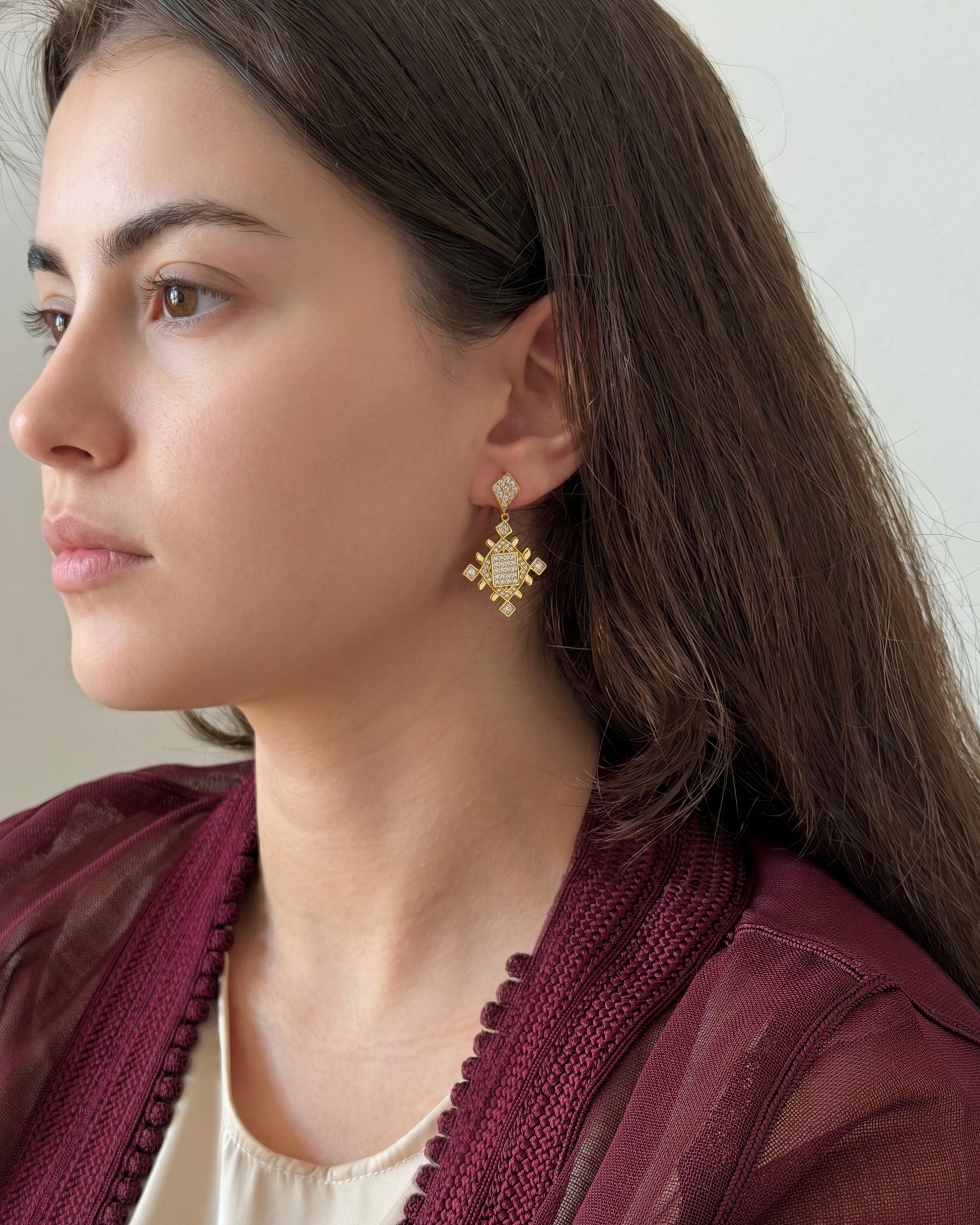 Lifestyle photo of a woman wearing gold Lion’s Paw statement earrings with a burgundy heritage-inspired look.