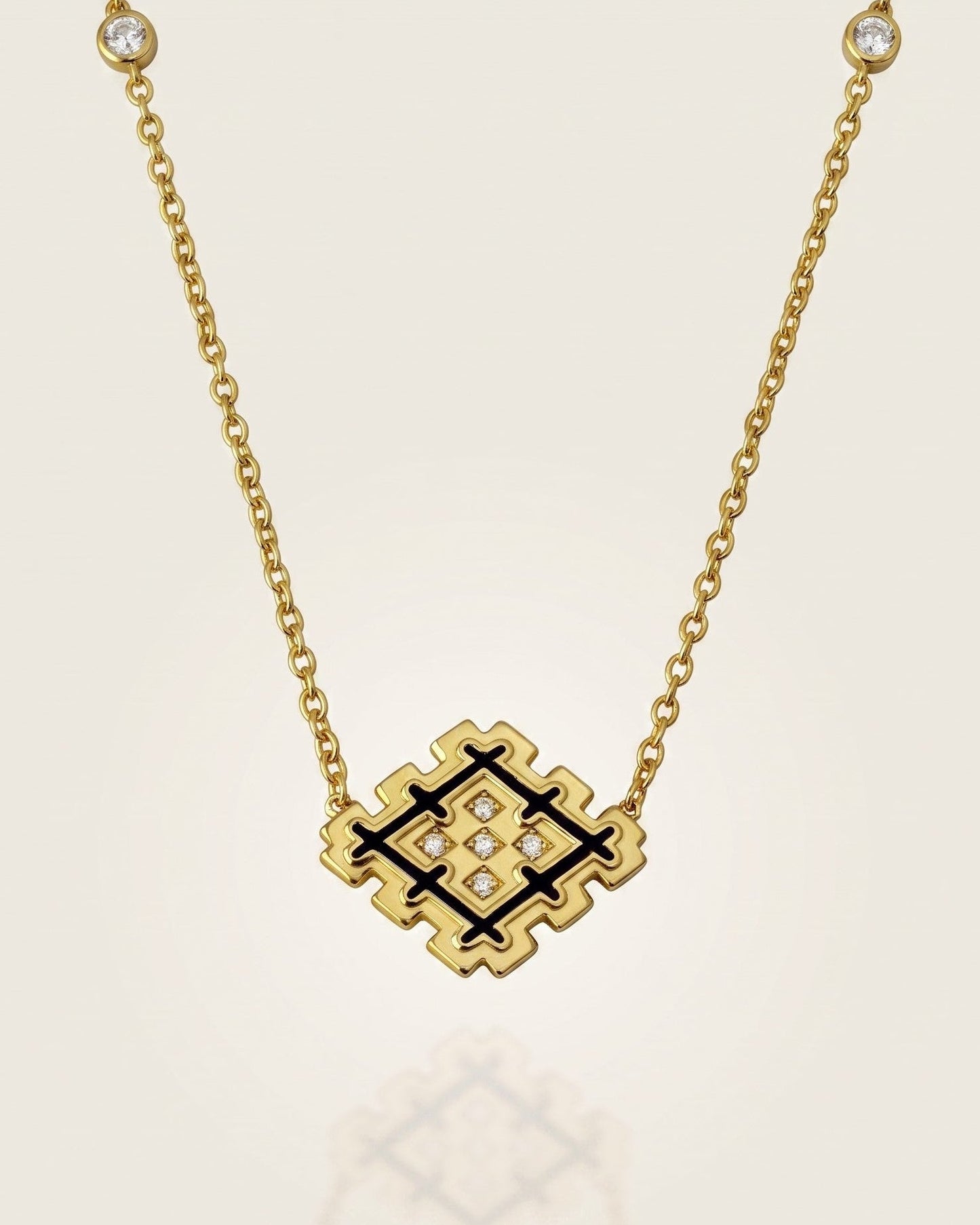 Gold vermeil Lion’s Paw necklace with black enamel and sparkling zirconia details, displayed against a soft neutral background with subtle reflection.