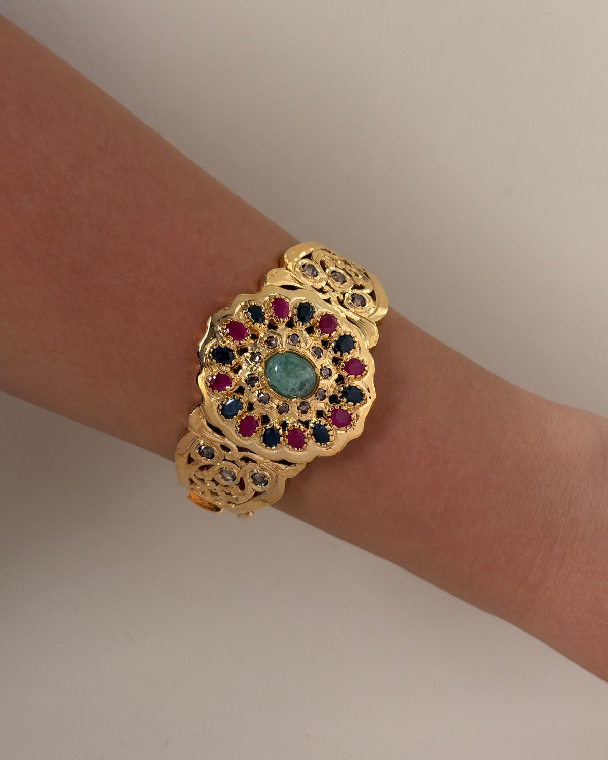 Close-up of the Moroccan bracelet worn on a wrist, showing its multicolour floral medallion and openwork band.