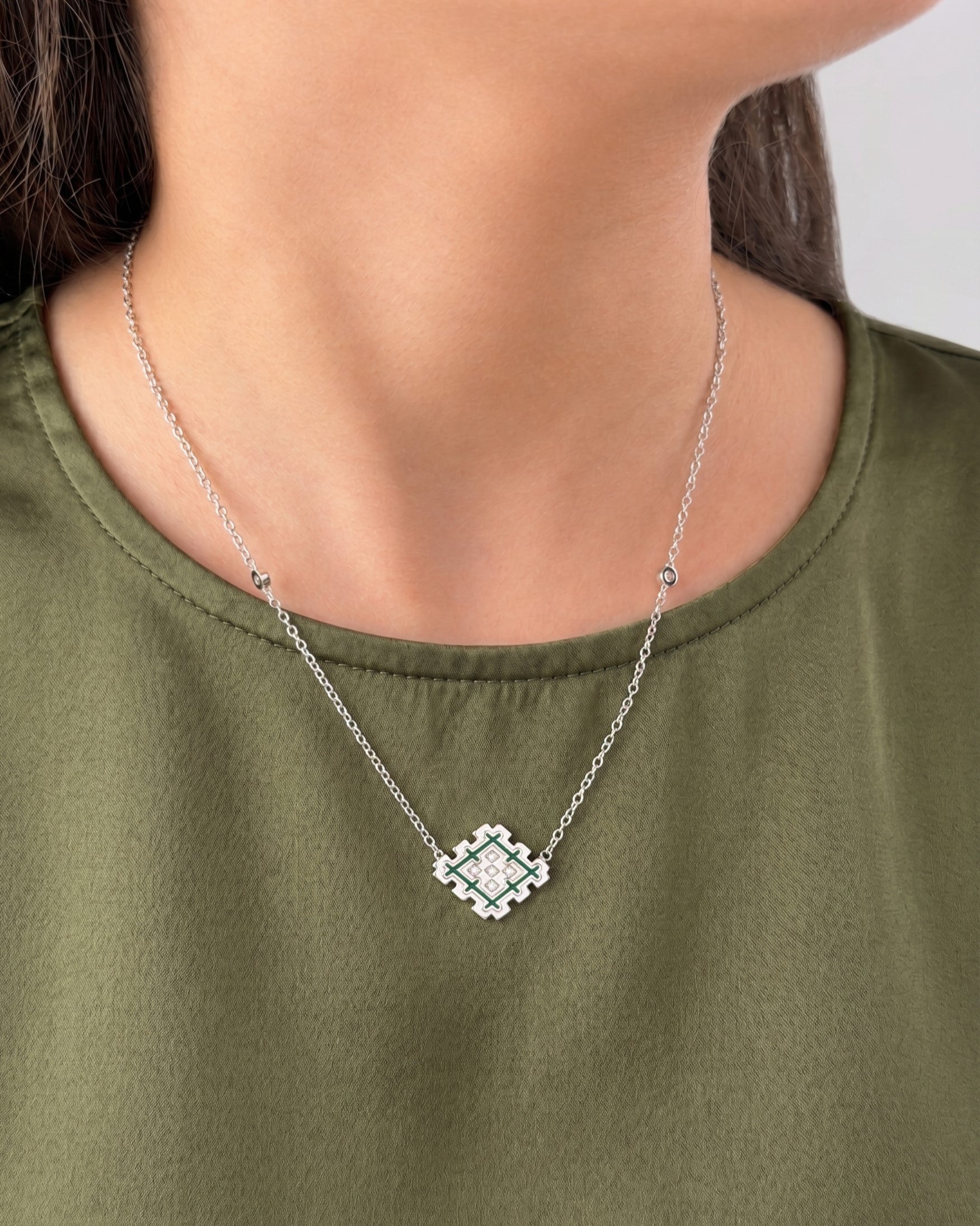 Woman wearing a silver Lion’s Paw green enamel necklace, styled with an olive top to show the pendant size and everyday look.